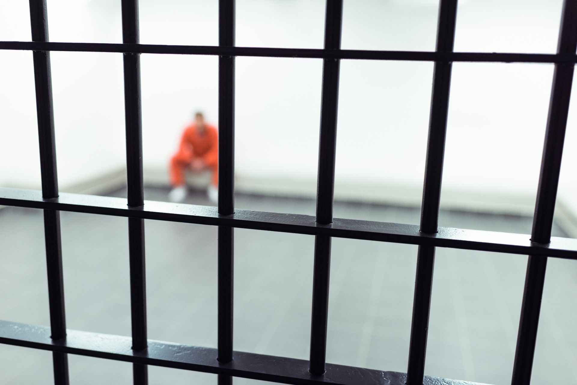 Blurred image of prisoner sitting alone in cell, with bars in foreground - prison visits