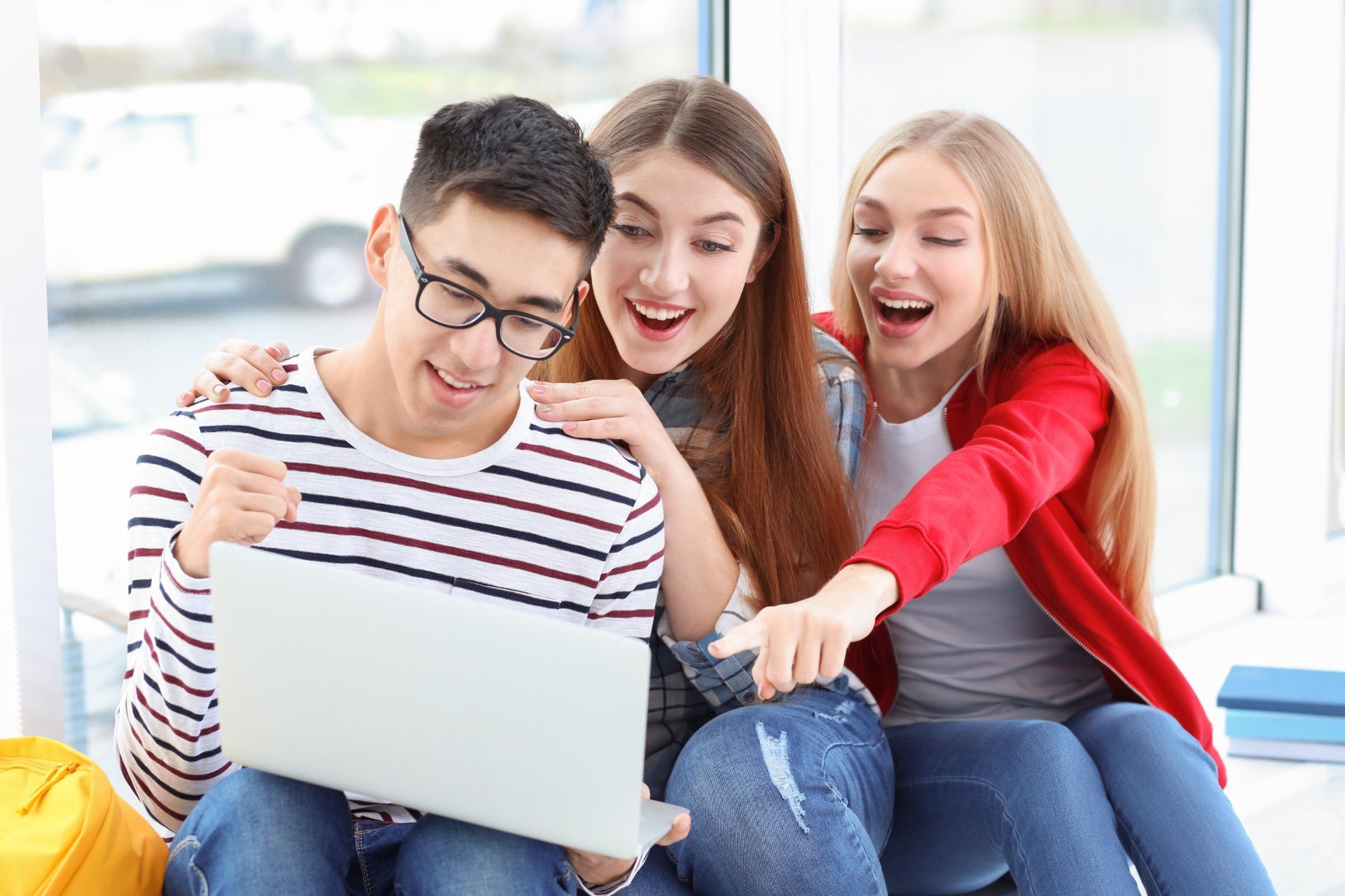 A male student holding a laptop and two female students cheer as they check their grades - A-levels