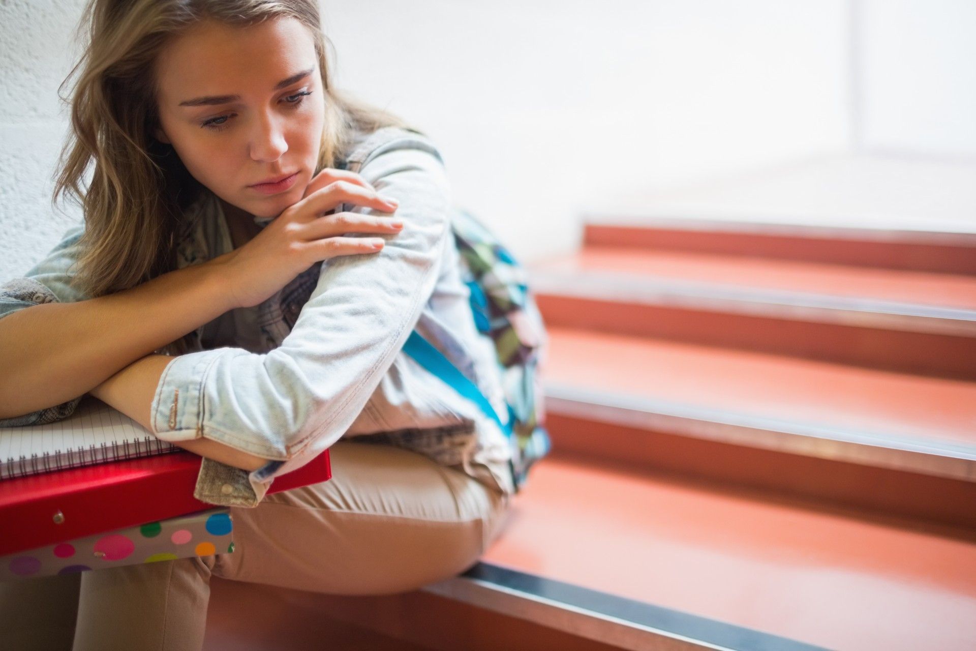 Upset teen girl sits in school stairwell with notebook and binder - A-level exam grades