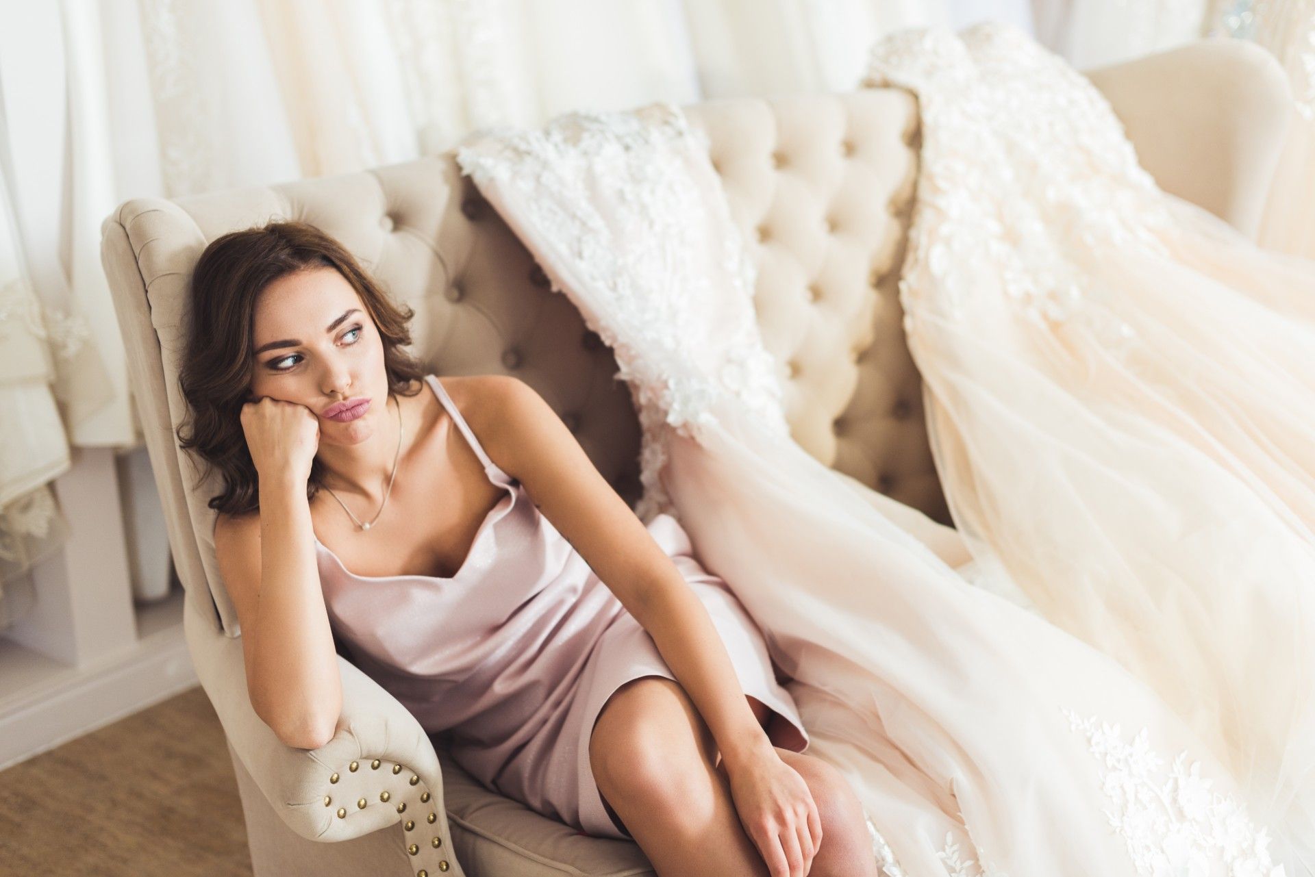 Annoyed woman sits in bridal shop with dresses lying next to her across the loveseat - cancelled weddings