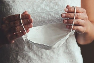 Closeup of bride's hands holding a white face mask - cancelled wedding