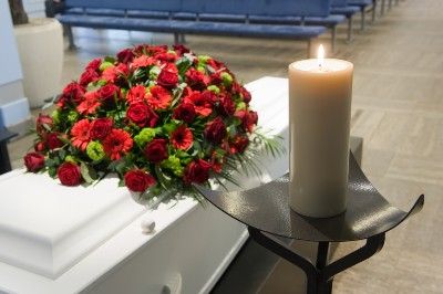 White casket with red roses on top and candles nearby in a funeral home - funeral cost