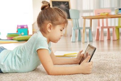 A little girl lies on the floor while watching something on a tablet - youtube class action lawsuit
