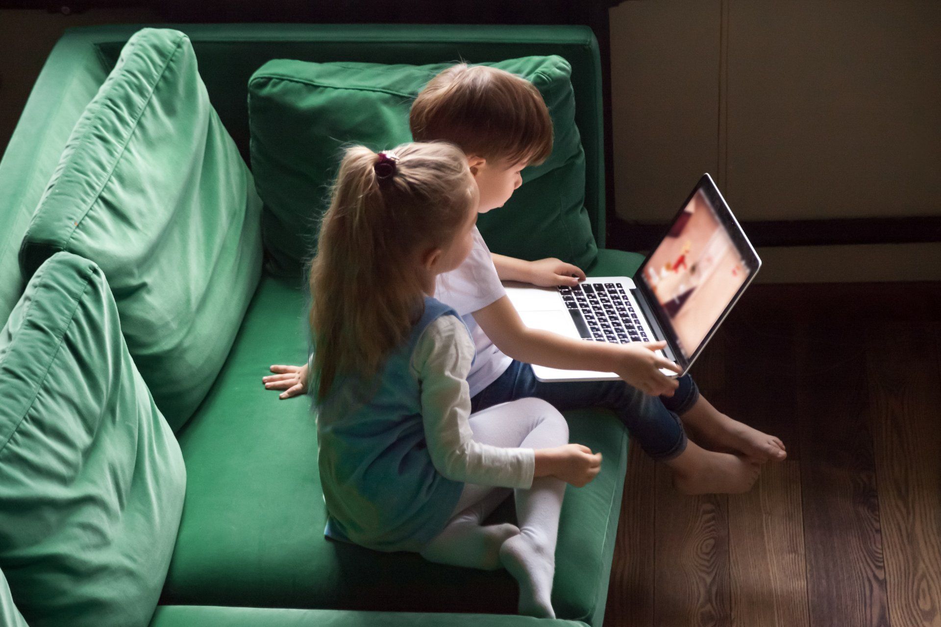 A young boy and girl sit on a green sofa while watching a video on a laptop - youtube class action lawsuit