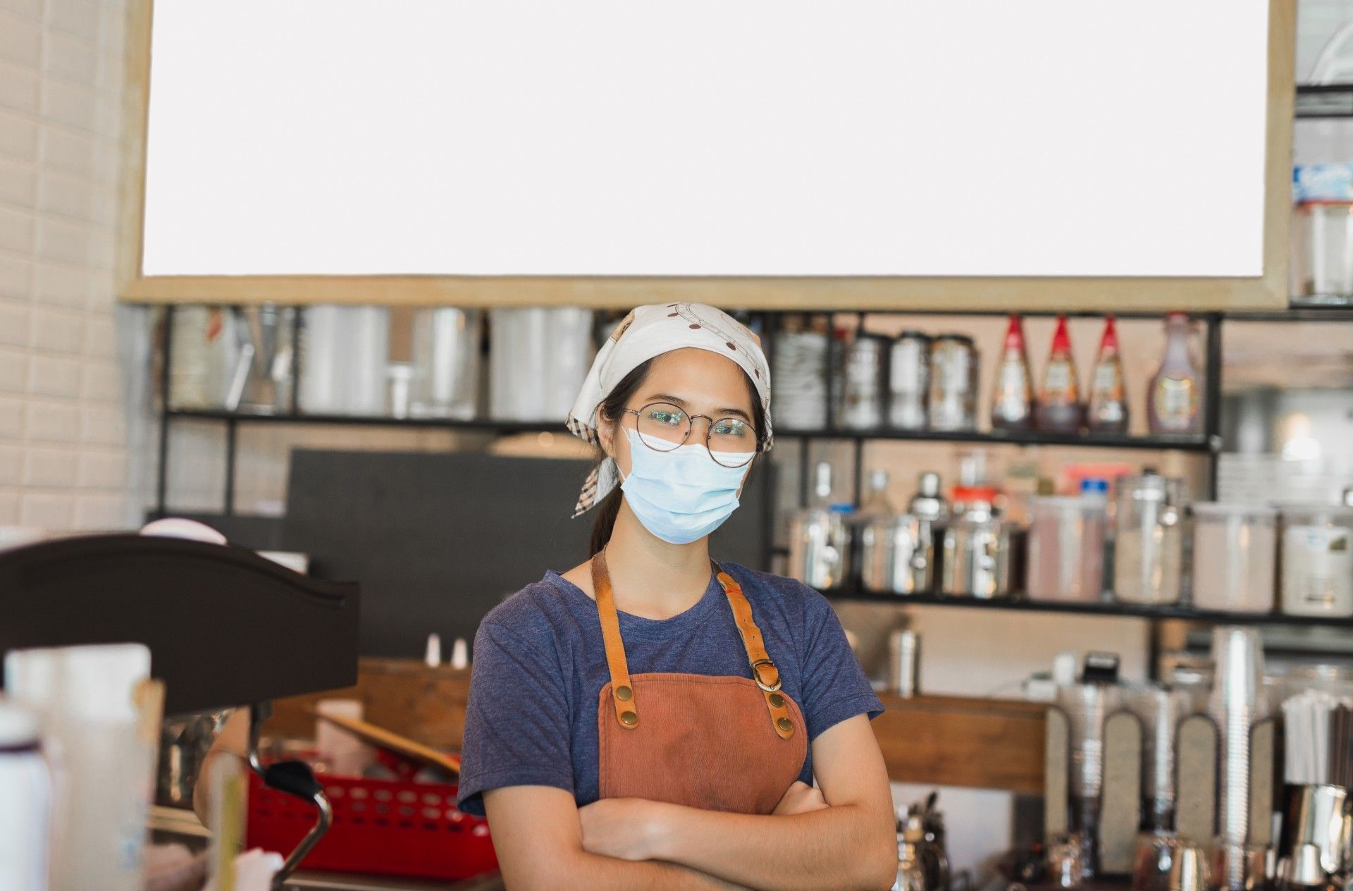 A female employee wearing a face mask and apron stands in a cafe - jobs scheme