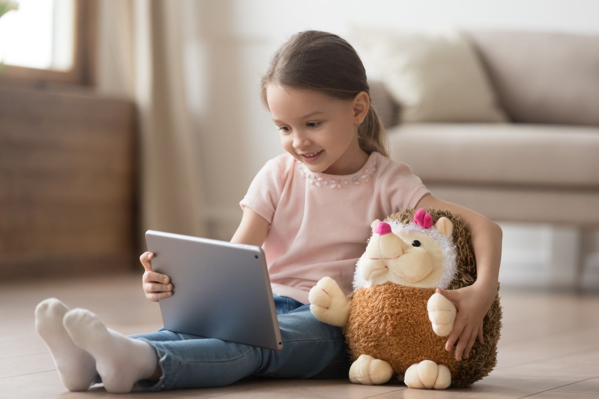 A young girl holds a stuffed hedgehog while sitting on the floor watching something on an ipad - youtube privacy