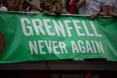 People stand near green "Grenfell Never Again" banner - cladding