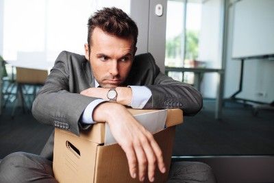 Man in suit sits with box of desk contents after being fired - jobs scheme