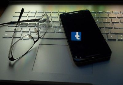 Glasses next to smartphone on laptop keyboard, with Facebook logo reflected upside down on smartphone screen - cambridge analytica ceo