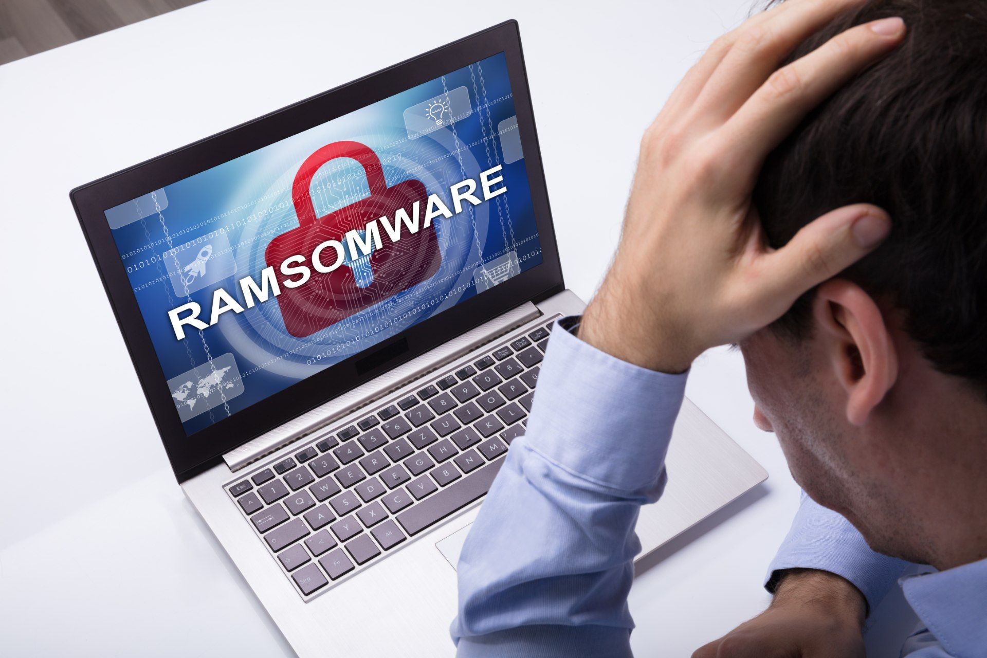 A man sits with his head in his hand while looking at a "ransomware" screen on his laptop - blackbaud ransomware attack