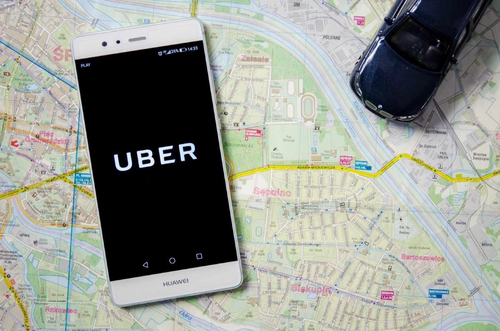 Smartphone showing Uber app lies on top of map with model car - london licence