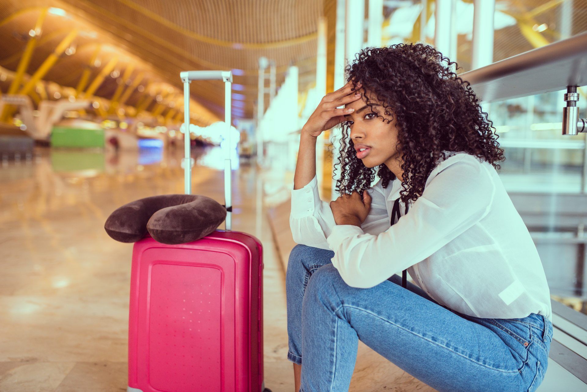 A frustrated woman sits with her head in her hand in an airport with her suitcase - tui uk