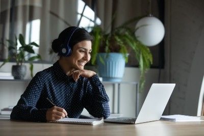 Woman wears headphones and works from home on a laptop - return to work