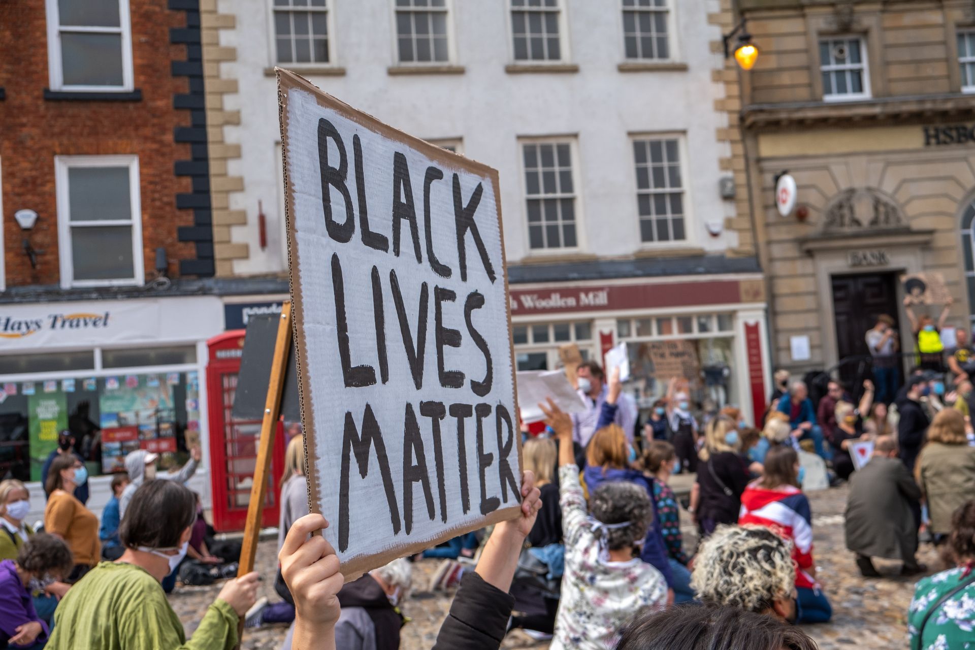 Richmond, North Yorkshire, UK - June 14, 2020: A Black Lives Matter placard is held up above a kneeling crowd at a protest in Richmond, North Yorkshire — BLM UK
