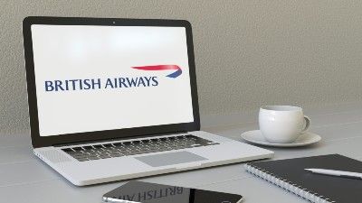 British Airways screen is up on a laptop next to a smartphone, notebook with pen, and cup of coffee - british airways fine