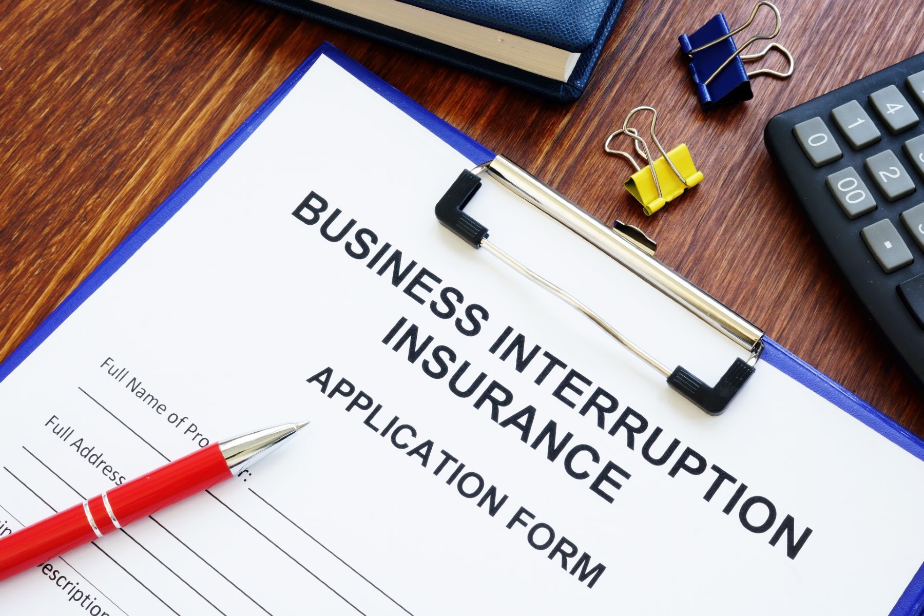 A clipboard holding a business interruption insurance application form, surrounded by clips, a pen and a calculator - business interruption test case