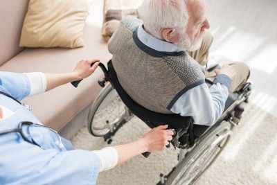 A young medical worker pushes an elderly man in a wheelchair - glenabbey manor