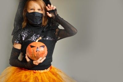 A girl in a black-and-orange Halloween costume wears a mask - halloween safety tips