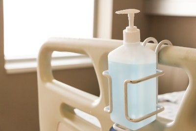 A bottle of hand sanitiser hangs on the end of a hospital bed - virapro hand sanitiser