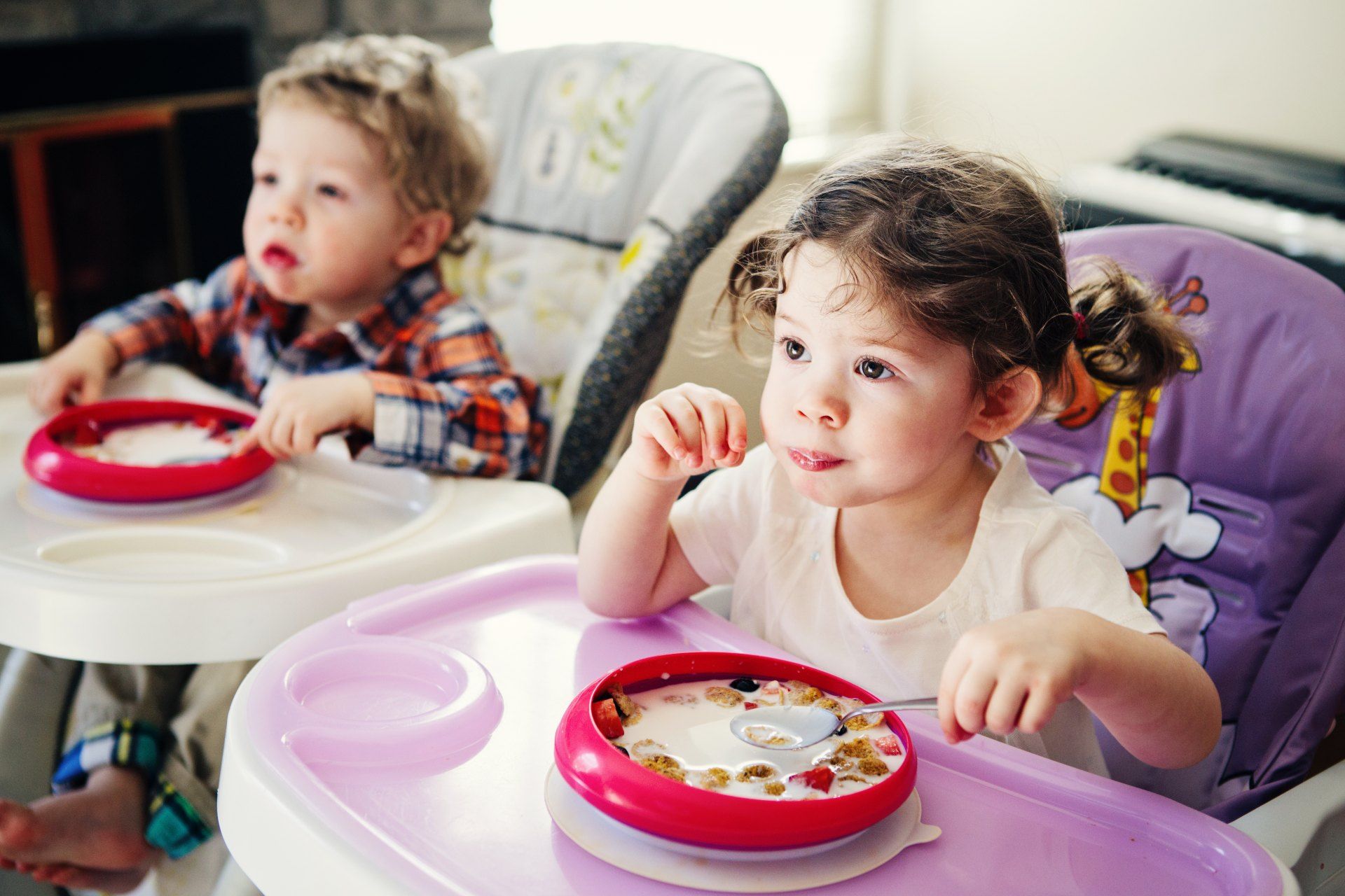 A young boy and girl sit in high chairs while eating cereal - cuggl high chair recall