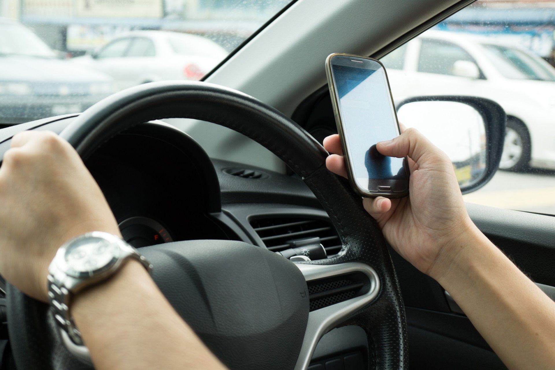 A driver holds the wheel with one hand and uses a mobile phone with the other - mobile phone driving ban