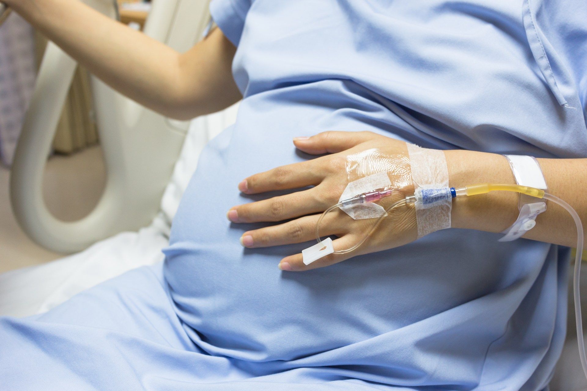 Closeup of a pregnant woman's arm and abdomen as she sits wearing a blue gown in a hospital bed - primodos victims