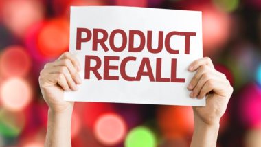 Closeup of a person's hands holding up a sign that reads "Product recall"; blurry colored lights in the background - baker ross toys