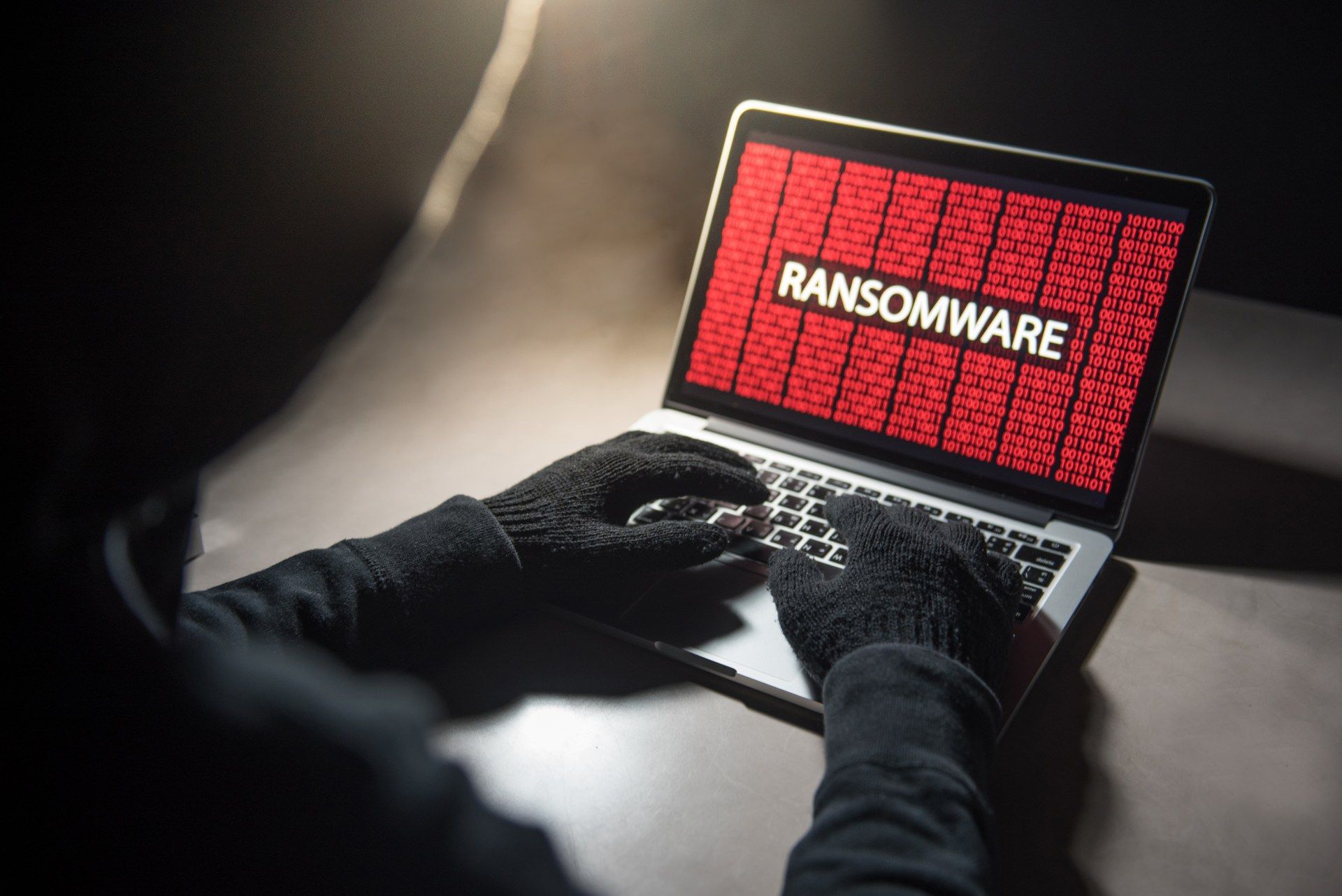A hacker in black installs ransomware using a laptop - blackbaud ransomware attack