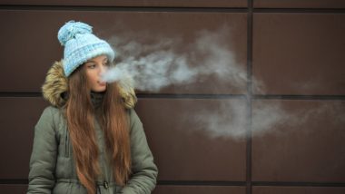 A teen girl in a coat and blue winter hat vapes - vape samples
