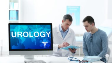A doctor talks with a patient in the background, with a computer in the foreground with a screen that says "urology" - Craigavon Area Hospital