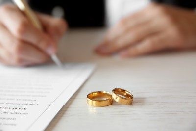 Gold wedding bands lie next to a person signing a marriage document - civil partnerships