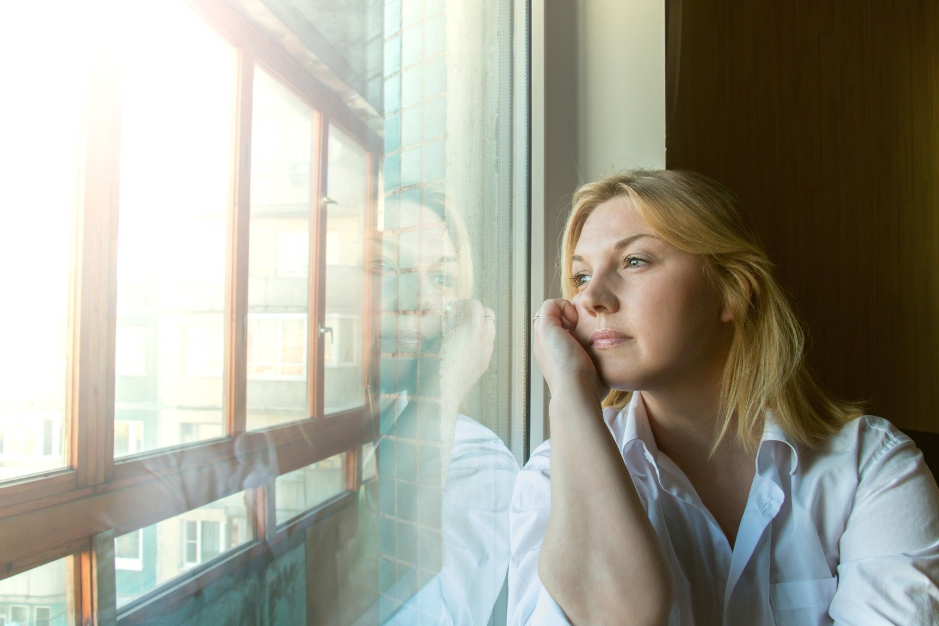 Woman deep in thought looks out a window - circuit breaker lockdown