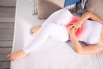 A woman in white grabs her lower abdomen; a red graphic indicates where her pain is - Essure implant