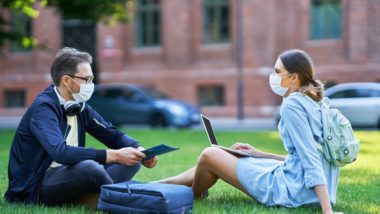 Two students wearing masks sit on the lawn at university - u.k. universities reopening