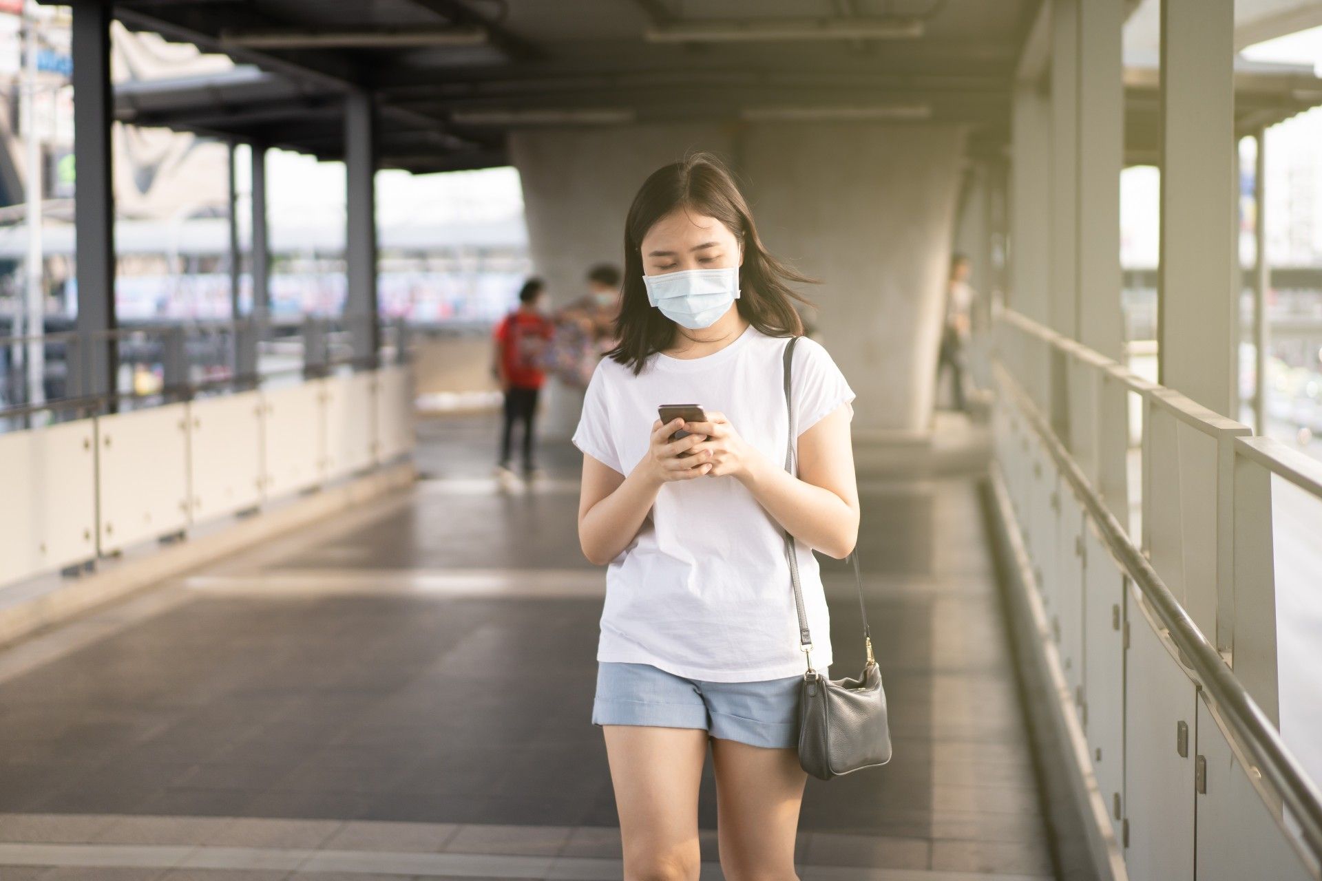 A woman walks while wearing a mask and looking at her smartphone - test and trace app