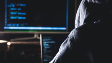 A hacker in a hoodie sits at two computer monitors - 118 118 money