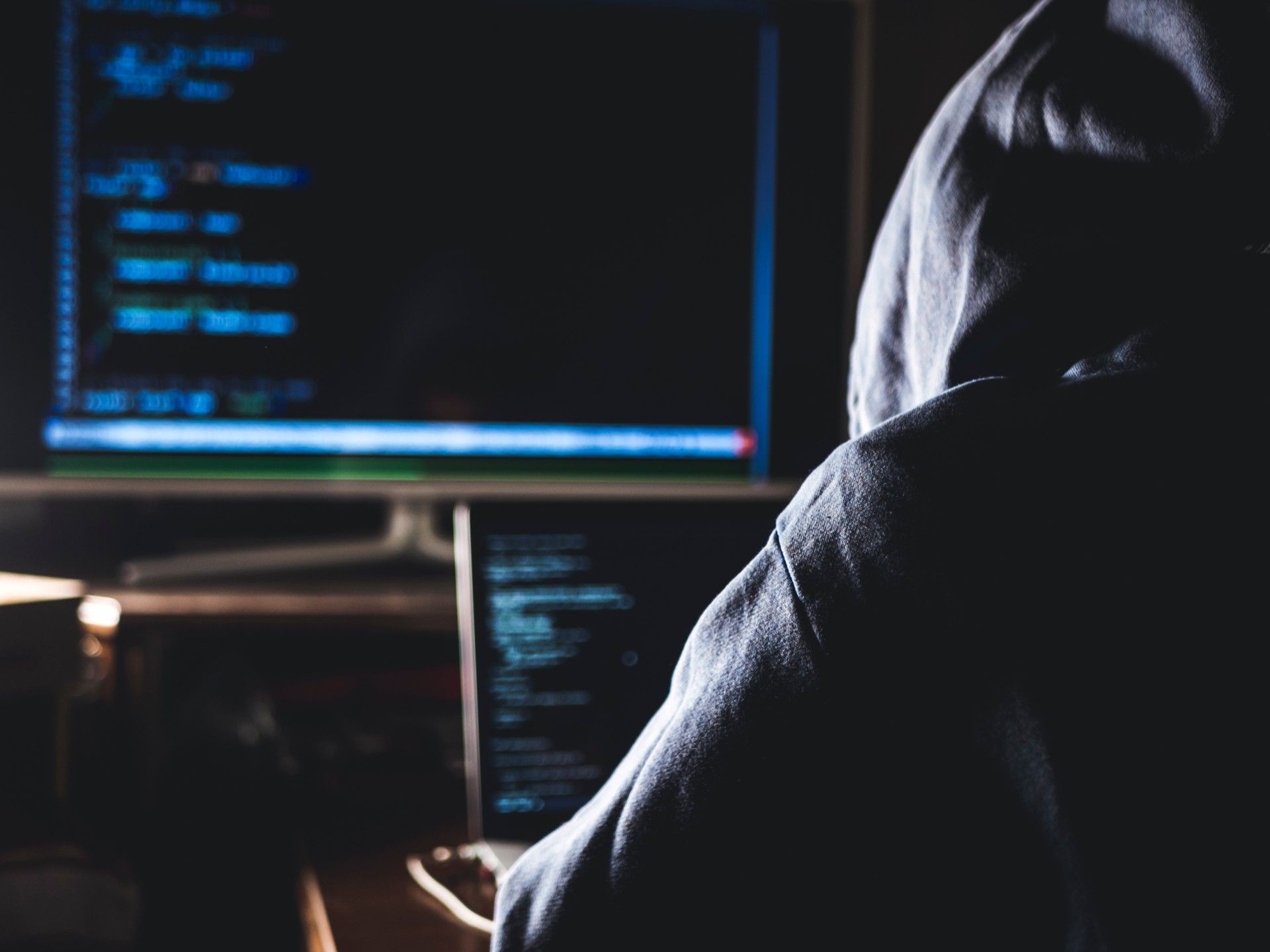 A hacker in a hoodie sits at two computer monitors - 118 118 money
