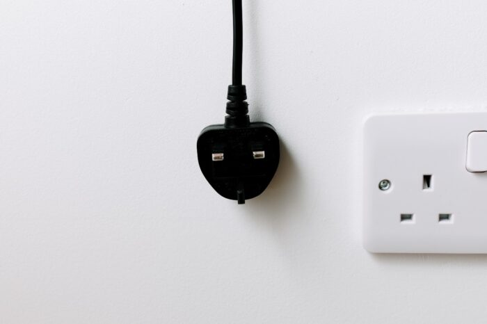 A black plug from the United Kingdom is hanging on white background. energy crisis concept.