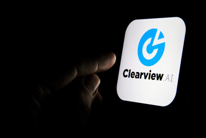 Clearview AI facial recognition software logo on the glowing screen and the finger pointing at it.