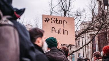 People in the streets protesting against war. A sign reads '#Stop Putin.'