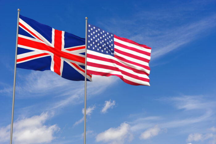 US and UK flag waving in the wind against a blue sky.