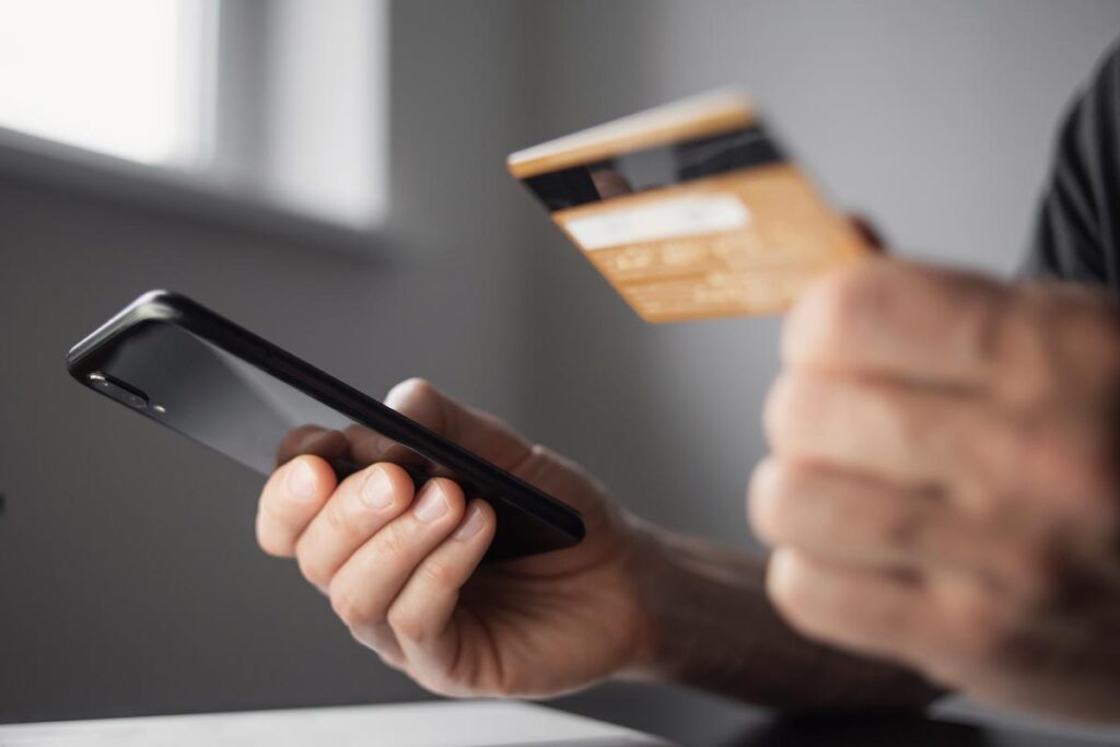 Close up of a man holding a debit card and a smartphone, representing UK push payment fraud reimbursement.