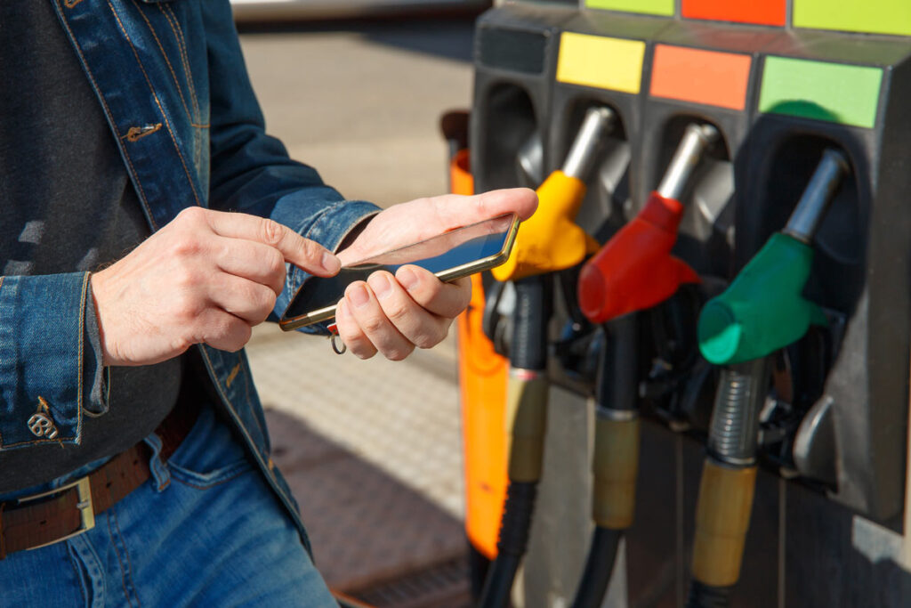 Person using smartphone with gas pumps in the background, representing the proposed UK fuel finder.