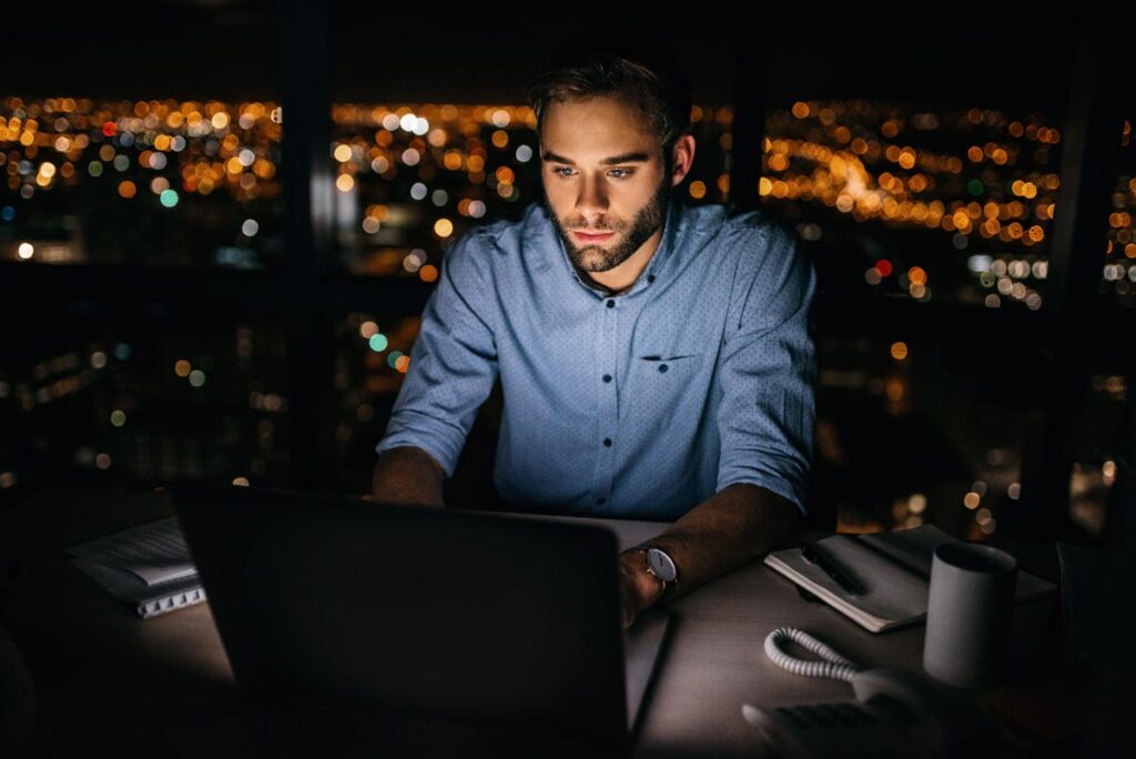 A young businessman working on his laptop at night, representing the unpaid overtime survey.
