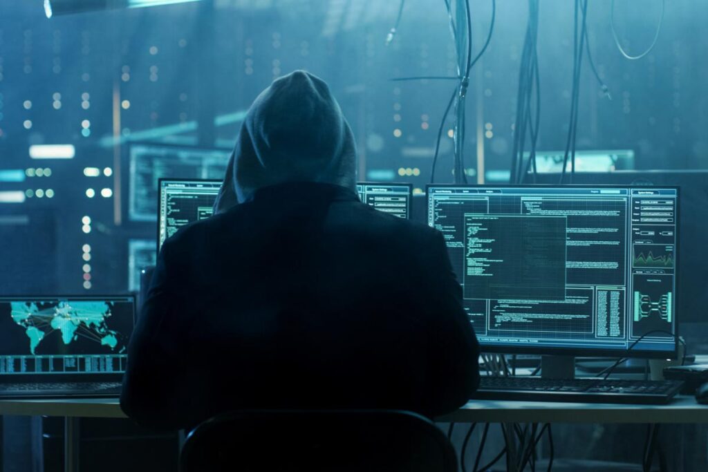 Back view of a hooded hacker using a computer, representing the Electoral Commission hack.