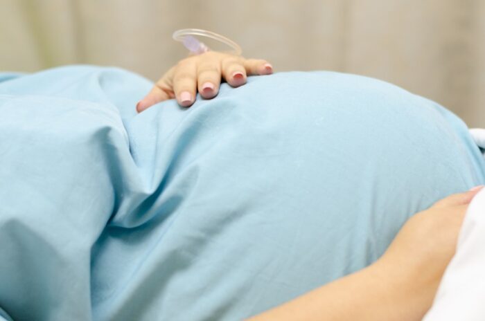A close up of a women where she is holding her pregnant tummy, and you can see a drip in her hand.