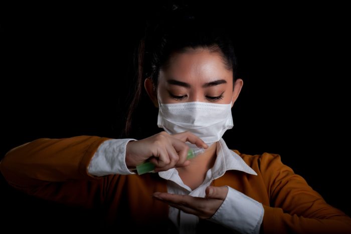 Woman wearing mask and applying hand sanitizer regarding Health Canada issuing a warning to consumers about fraudulent N95 respirators and lifting restrictions on technical-grade ethanol