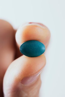 Fingers holding a pill up close regarding information on Truvada side effects 