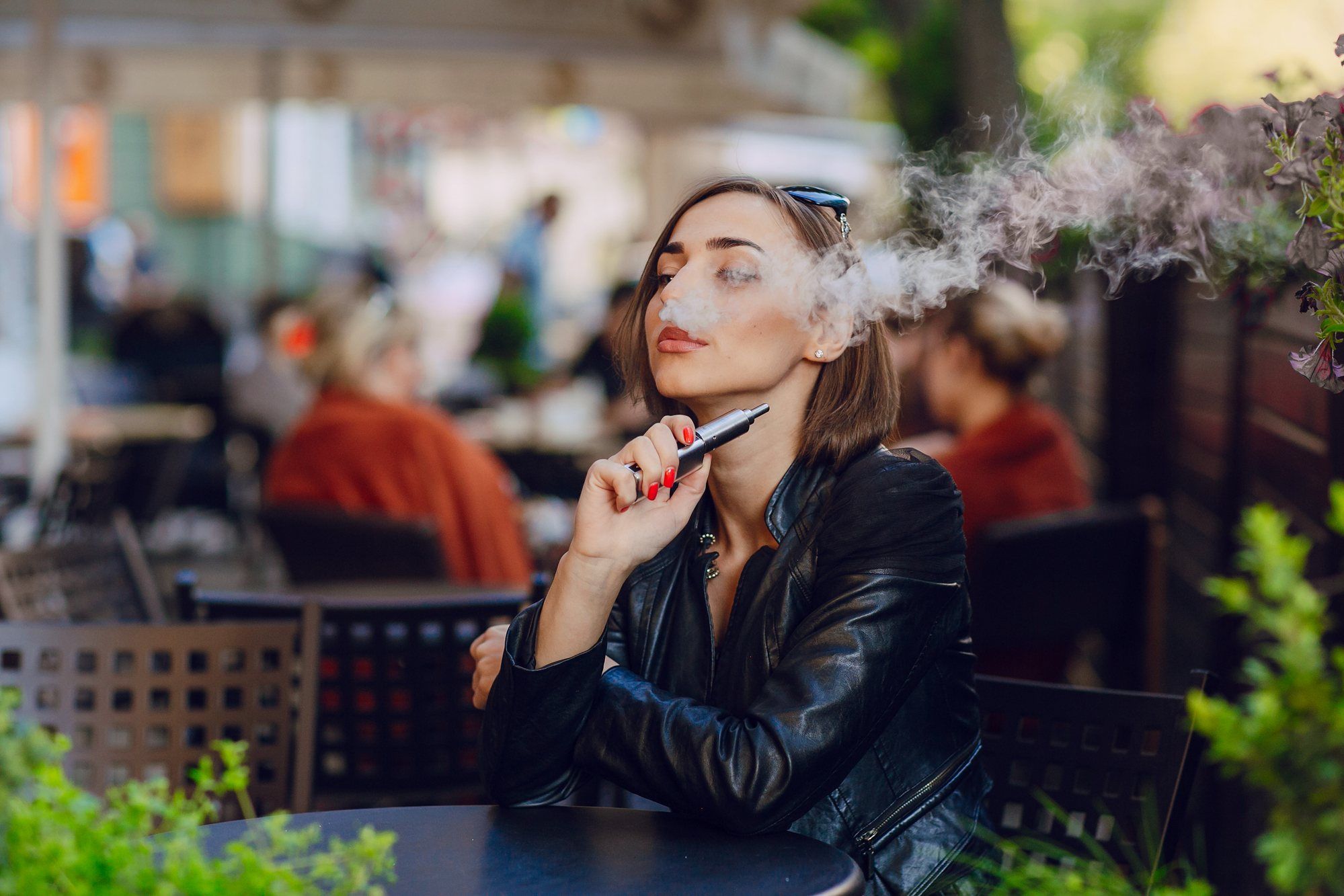 Woman blowing smoke while vaping at table regarding information on whether JUUL e-cigarettes are bad for you