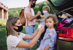 Family putting on masks by car regarding the COVID-19 travel ban class action lawsuit filed